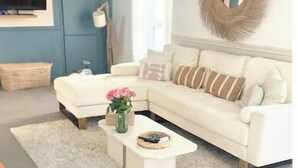 Una sala de estar moderna con un sofá blanco, una mesa de centro con flores y un espejo redondo en la pared.