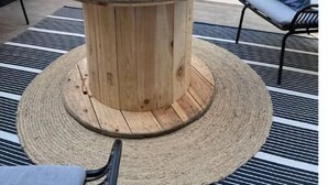 Una mesa redonda de madera con base tejida, rodeada por un tapete a rayas.