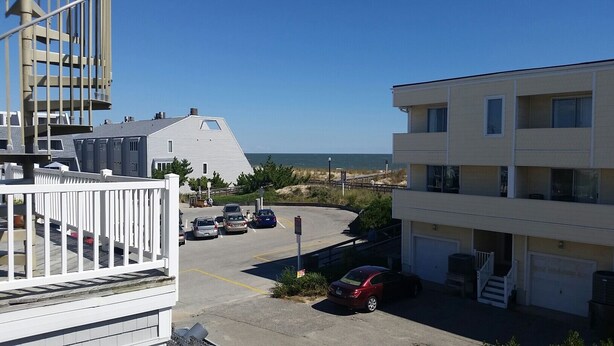A coastal building with a parking area, a white fence, and a view of the ocean. - Bethany Beach 6 BR with Elevator - one house back from the beach (Bethany Beach)