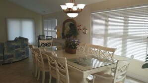 A dining area with a glass table and white chairs, a chandelier, and a potted plant. - Bethany Beach 6 BR with Elevator - one house back from the beach (Bethany Beach)