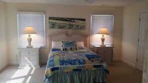A bedroom with a bed, two nightstands, two lamps, a painting, and a door. - Bethany Beach 6 BR with Elevator - one house back from the beach (Bethany Beach)