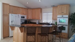 A kitchen with wooden cabinets, a refrigerator, a microwave, a sink, and a bar area with chairs. - Bethany Beach 6 BR with Elevator - one house back from the beach (Bethany Beach)