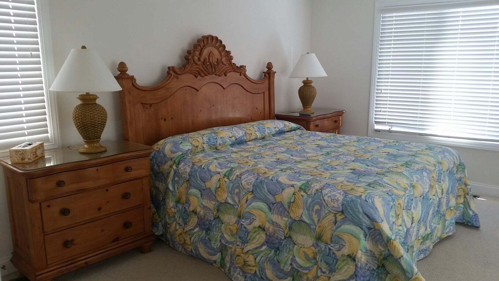 A bedroom with a wooden bed, two bedside tables, a dresser, and a window with blinds.