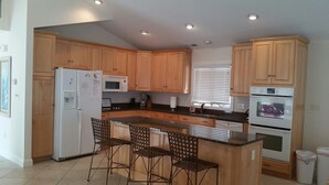 A kitchen with wooden cabinets, a refrigerator, microwave, oven, and a bar area with chairs. - 6 Bedroom with an elevator one house back from the beach! (Bethany Beach)