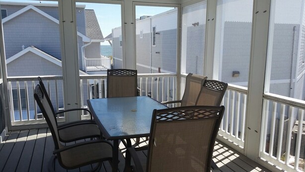 A covered outdoor patio with a table and chairs, overlooking a residential area. - 6 Bedroom with an elevator one house back from the beach! (Bethany Beach)