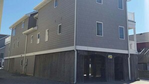 A multi-story building with a garage entrance, a small balcony on the upper floor, and a clear sky. - 6 Bedroom with an elevator one house back from the beach! (Bethany Beach)