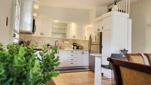 Une cuisine moderne avec des meubles blancs, un réfrigérateur en acier inoxydable et un coin repas comprenant une table et des chaises.
