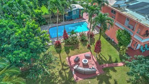 Une piscine entourée d’une végétation luxuriante, une terrasse avec des meubles d’extérieur et un bâtiment doté de balcons.