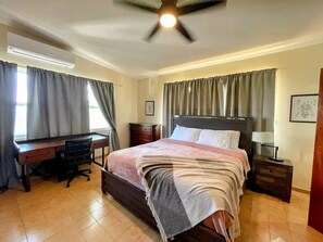 Comfortable retreat with a large bed, desk, and nightstand, featuring a ceiling fan and tiled floor.