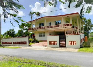Stunning two-story residence with a balcony and symmetrical facade, set amidst lush green surroundings.