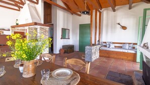 Un comedor rústico con una mesa de madera dispuesta para dos comensales, un banco de piedra y una puerta verde al fondo.