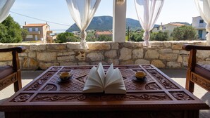 Una mesa de madera con un libro abierto y dos tazas, frente a una pared de piedra con vistas a casas y montañas.