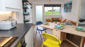 A compact kitchen with a toaster, a sink, and a dining area with a table set for two. - Nanny's Little House (Sandown)