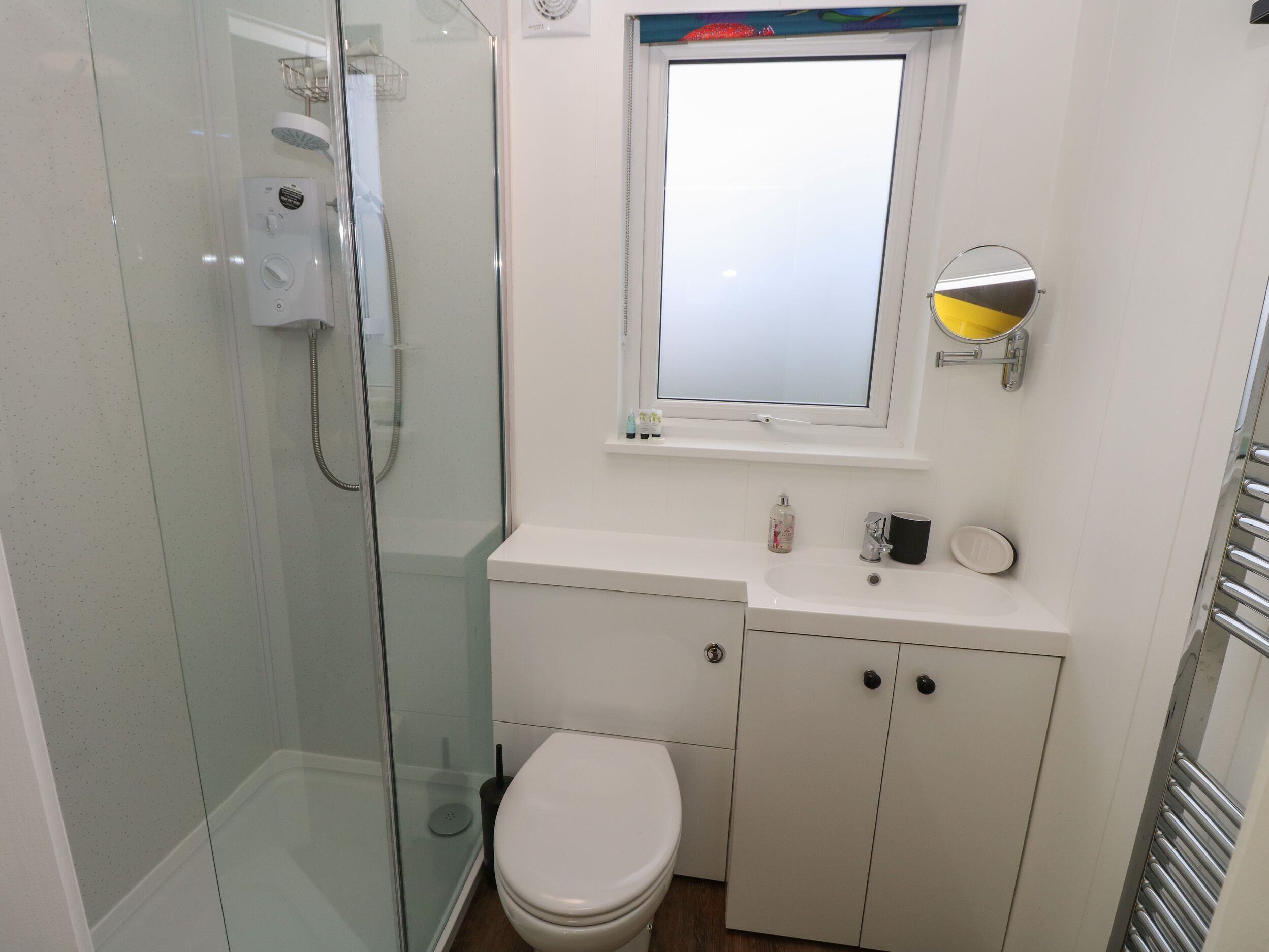 Un baño moderno con ducha de vidrio, inodoro blanco y lavabo con espejo superior.