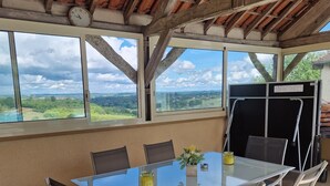 A dining area with a glass table and chairs, large windows, and a view of the countryside. - Gîte à la Campagne Avec Piscine (Sarlat-la-Canéda)