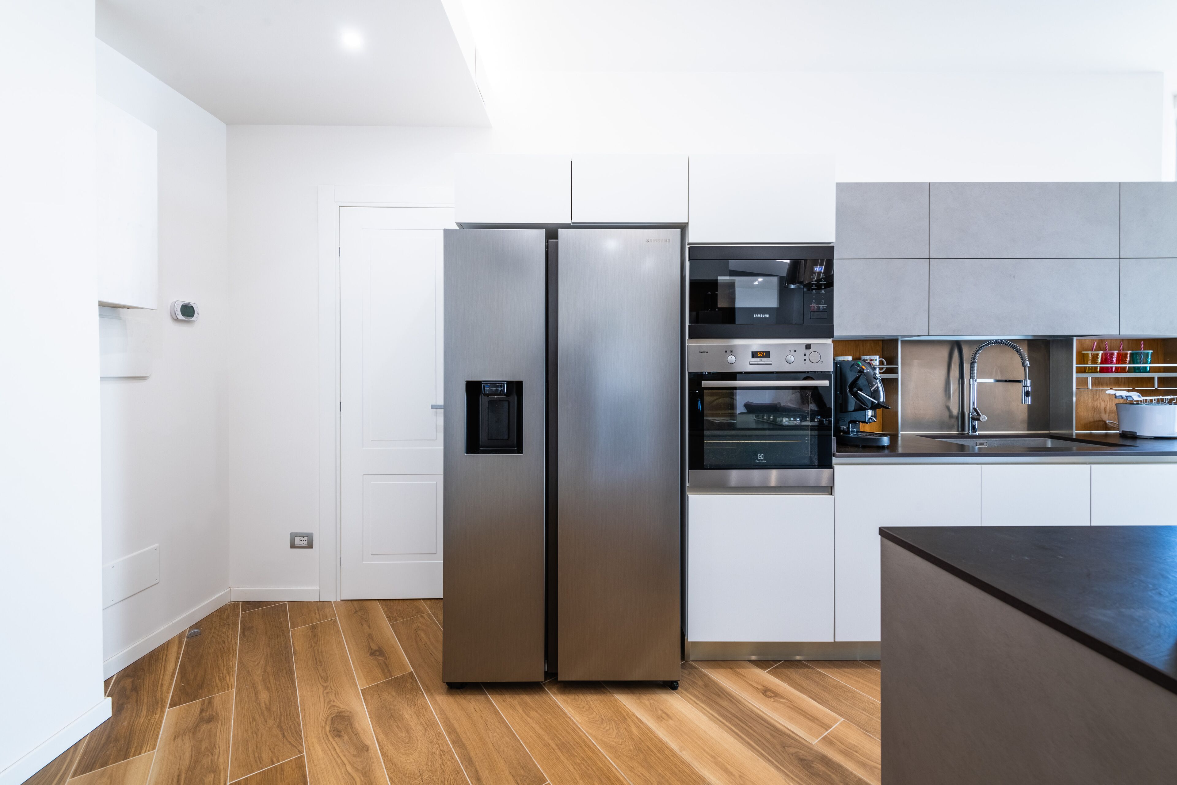 A modern kitchen with stainless steel appliances, a wooden floor, and white cabinetry.