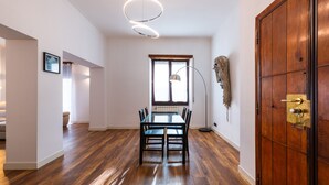 Ein geräumiges Zimmer mit Holzboden, einem Esstisch mit Stühlen, einer großen Holztür und einem Fenster mit Blick.