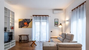 Ein Wohnzimmer mit einer Couch, einem Fernseher, einem Glastisch und einem Bild an der Wand.