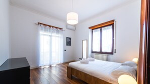 Ein Schlafzimmer mit einem hölzernen Bett, einem Nachttisch, einer Lampe, einem Heizkörper und einem Fenster mit Vorhängen.