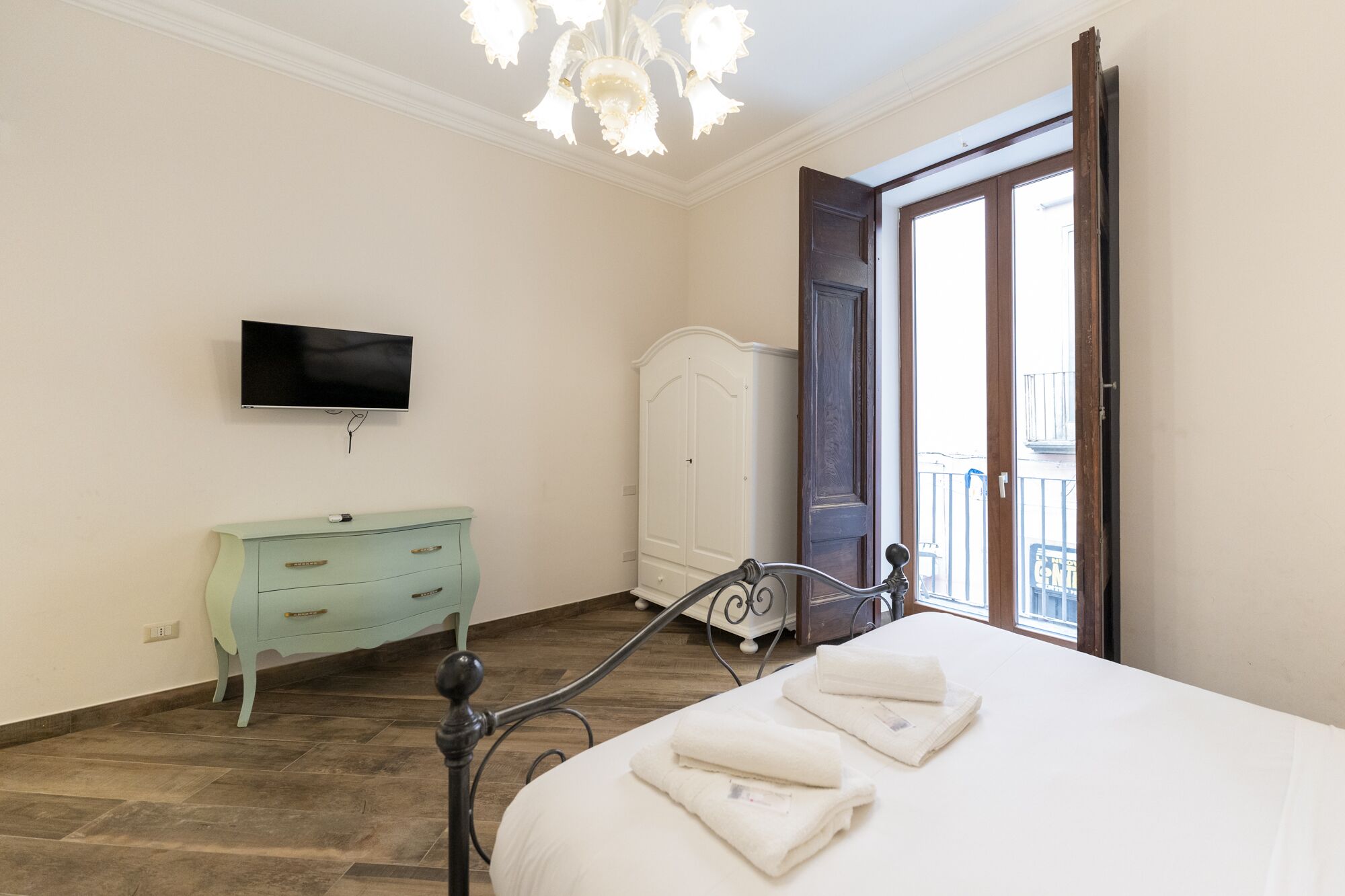 Quarto com cama, televisão, guarda-roupa e porta para varanda.
