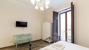 Ein Schlafzimmer mit Bett, Fernseher, Kleiderschrank und einer Tür zum Balkon.
