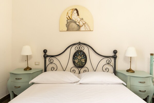 Un lit avec du linge de lit blanc, une tête de lit décorative, deux tables de chevet avec des lampes et un tableau accroché au mur.