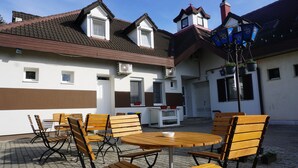 An outdoor seating area with wooden tables and chairs, a street lamp, and a building with a sloped roof and air conditioning units. - Május 1 Vendégház - Torony (Torony)