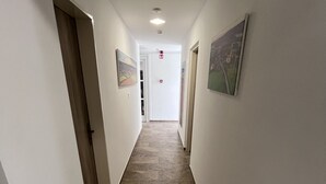 A narrow hallway with tiled flooring and white walls. There are doors on both sides and a fire alarm on the wall. - Május 1 Vendégház - Torony (Torony)