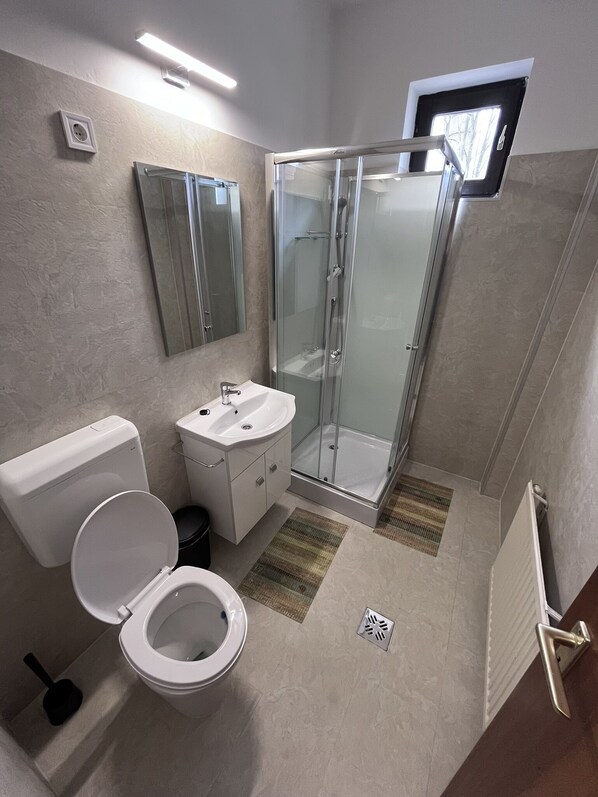 A modern bathroom with a toilet, sink, and glass-enclosed shower. - Május 1 Vendégház - Torony (Torony)