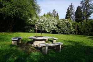 A stone outdoor seating area with a central table and benches, surrounded by lush greenery and flowering bushes. - Május 1 Vendégház - Torony (Torony)
