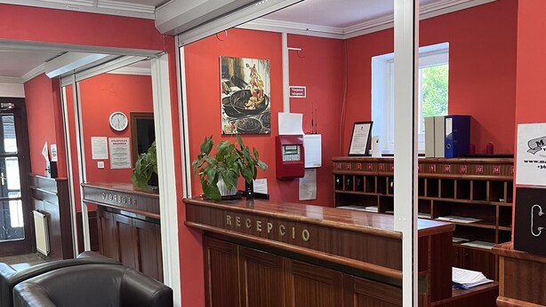 A reception area with a wooden reception desk, a black leather chair, a potted plant, and a clock on the wall. - Május 1 Vendégház - Torony (Torony)
