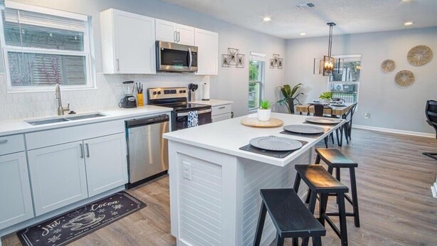 A modern kitchen with white cabinetry, a central island with stools, a microwave, and a coffee machine. - Charming Fenced 3BR/1BA Close to Vibrant Downtown (San Antonio)