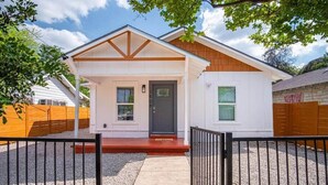 A single-story house with a front porch, a dark front door, and a small window. - Charming Fenced 3BR/1BA Close to Vibrant Downtown (San Antonio)