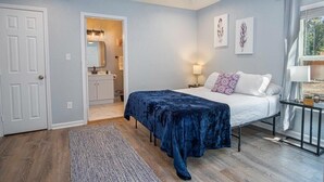 A bedroom with a bed, a ceiling fan, a nightstand, a window with curtains, and a door leading to a bathroom. - Charming Fenced 3BR/1BA Close to Vibrant Downtown (San Antonio)