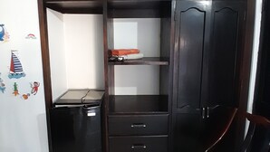 Une pièce avec une armoire en bois sombre, un petit bureau noir et une chaise verte rembourrée.