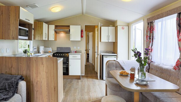 A compact RV kitchen with a microwave, stove, and oven, a dining area with a table and chairs, and a living space with a sofa.
