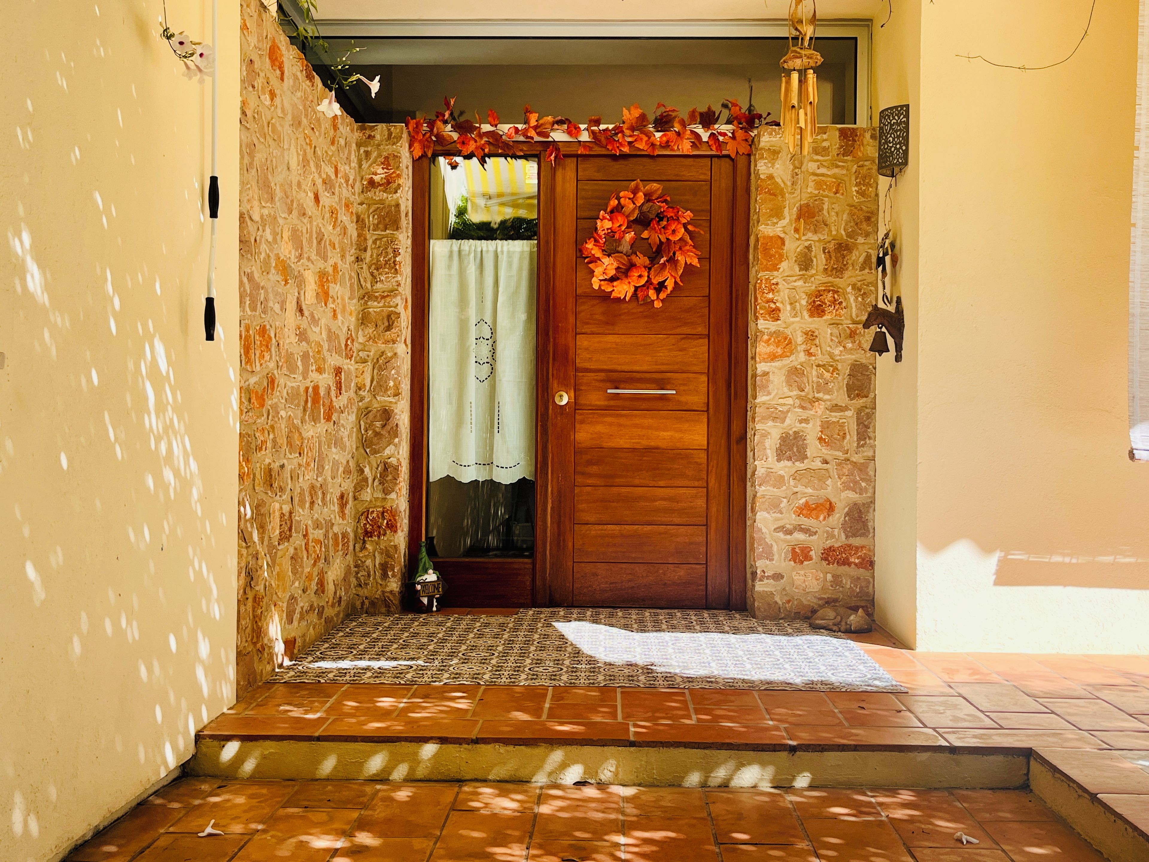 A stone-walled entrance with a wooden door, a patterned mat, and a wreath.