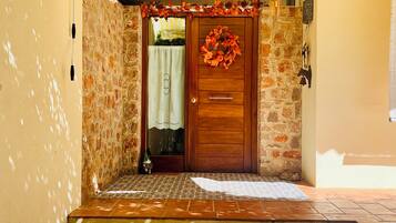 A stone-walled entrance with a wooden door, a patterned mat, and a wreath.