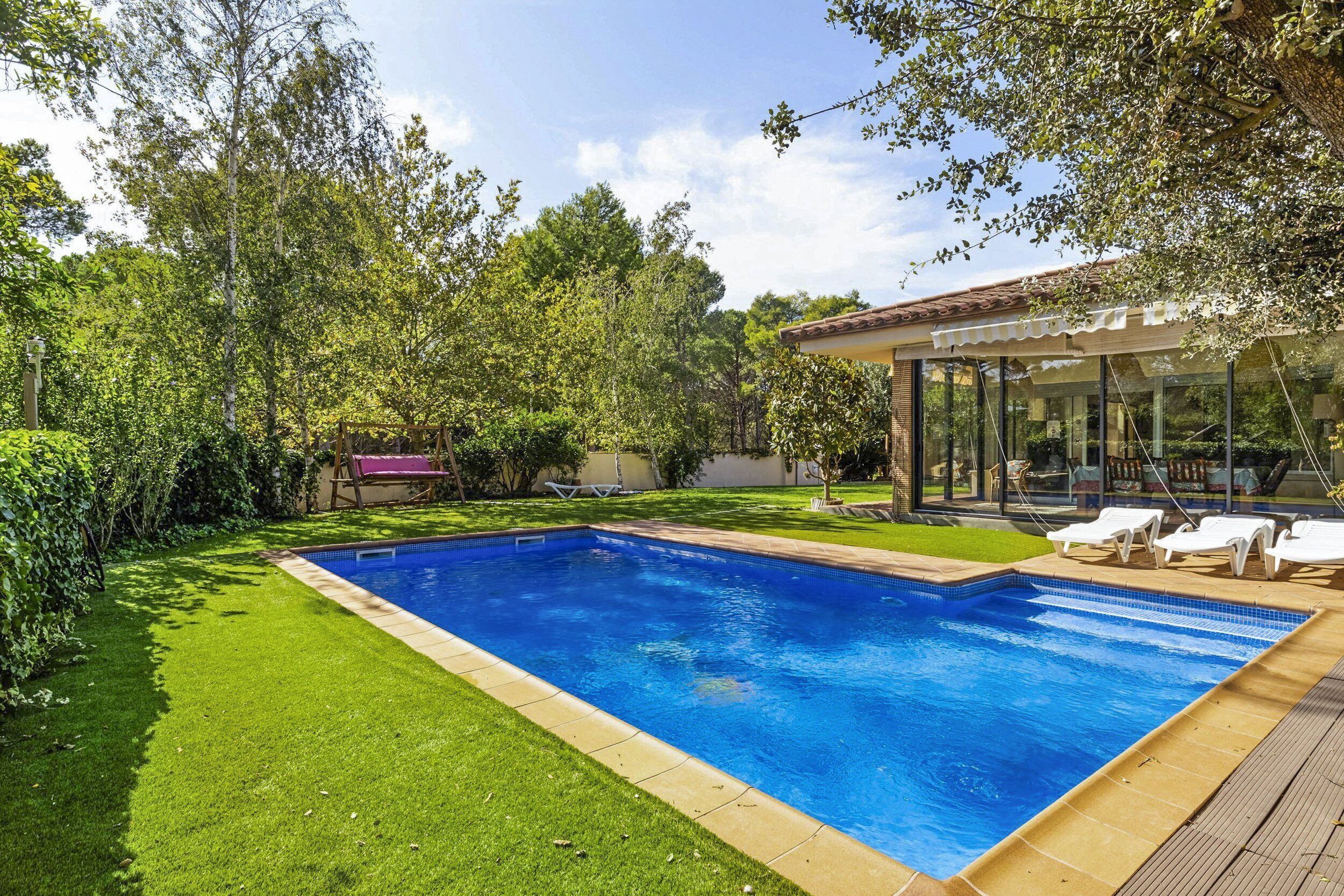 A rectangular swimming pool with a tiled edge, surrounded by a well-maintained lawn and trees.