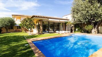 Una piscina con acqua cristallina e azzurra, circondata da un prato curato e un’area patio con lettini.