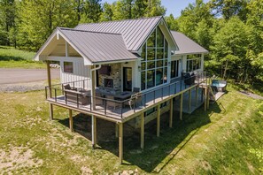 A two-story house with a deck, a fireplace, and a large window overlooking a forest. - Deep Creek Luxury w/ Pool, Theater & Fireplace (McHenry)