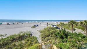 A beach with a sandy path leading to a wooden gate, palm trees, and beach umbrellas. - Oceanfront View @ A Place at the Beach 3 1I (Myrtle Beach)