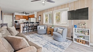 A living room with a sofa, patterned chairs, a coffee table, a TV, and a bookshelf with decorative items. - Oceanfront View @ A Place at the Beach 3 1I (Myrtle Beach)