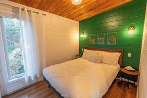 A bedroom with a wooden ceiling, a large bed, a window with white curtains, and a green wall with wall sconces.