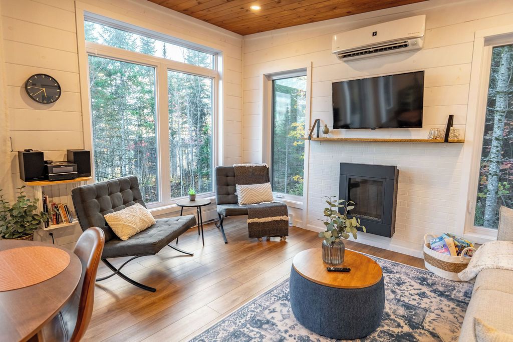 A modern living room with a fireplace, large windows, and a flat-screen TV.