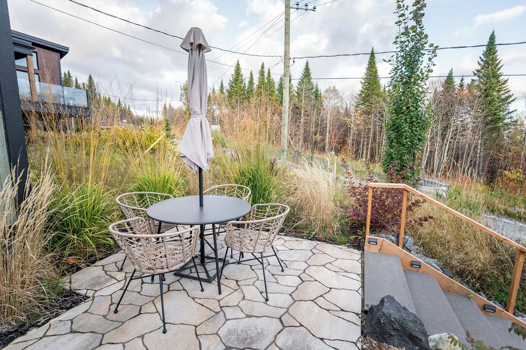 An outdoor patio with a round table and four wicker chairs, surrounded by stone flooring and a wooden staircase.
