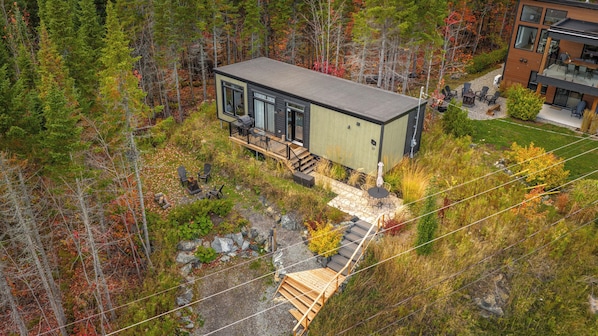 A modern cabin with a deck, surrounded by a forest.