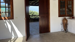 A room with a wooden door leading to a balcony, a potted plant, and a window with a view of greenery. - Finca la Hachita, Tranquilidad y Campo Cerca de Orotava y del Puerto de la Cruz (La Orotava)