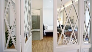 A hotel room with a wooden floor, a bed with white bedding, a grey sofa, and a small table. - Three Steps from Spanish Steps (Roma)