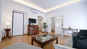 A spacious living room with a wooden coffee table, a sofa, a TV on a wooden cabinet, and a dining area with a table and chairs. - Three Steps from Spanish Steps (Roma)
